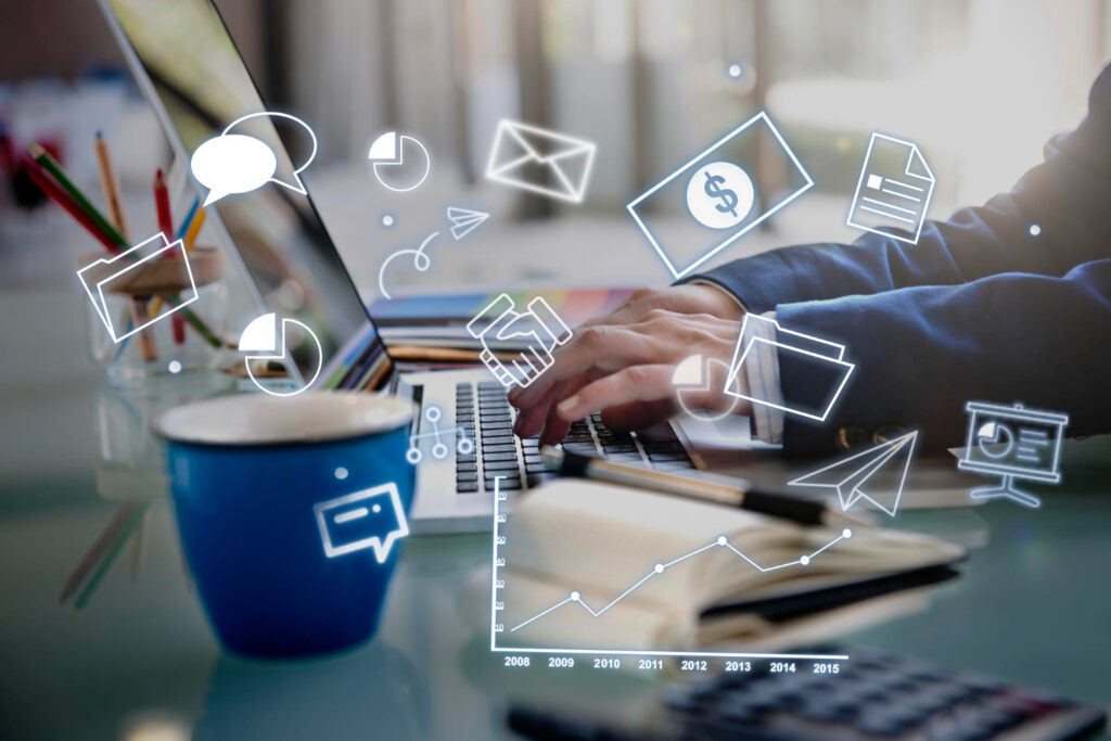 A businessman sitting at a desk using a laptop with various icons displayed on the screen and Digital marketing services